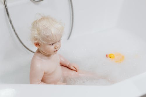 toddler calmly playing with bath toys in bathtub